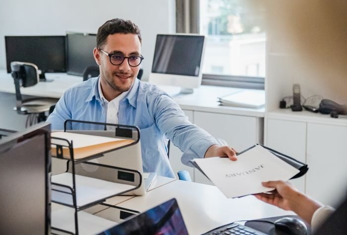 Two office workers exchanging documents in a bright office setting.